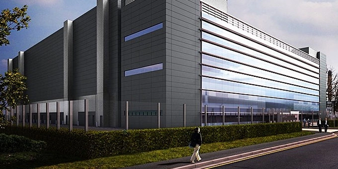 Exterior architectural rendering of a modern, multi-story data center building facility with a dark gray tiled facade, large glass windows, and a clean perimeter fence line.