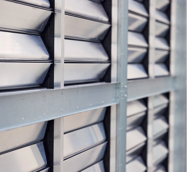 Close-up of an industrial fan wall or CRAH unit array, showcasing structured columns of metallic, aerodynamic louvers and dampers integrated into a galvanized steel framework.