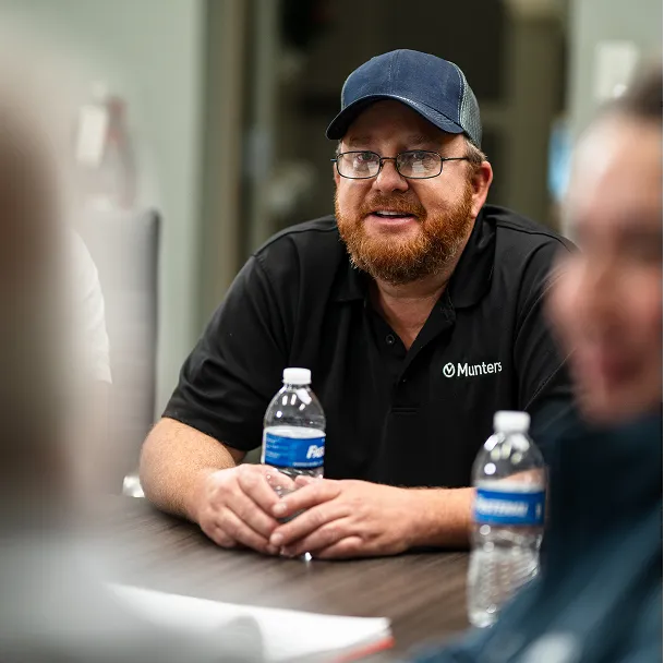 A Munters employee wearing a black polo shirt and baseball cap engaged in a meeting room discussion.